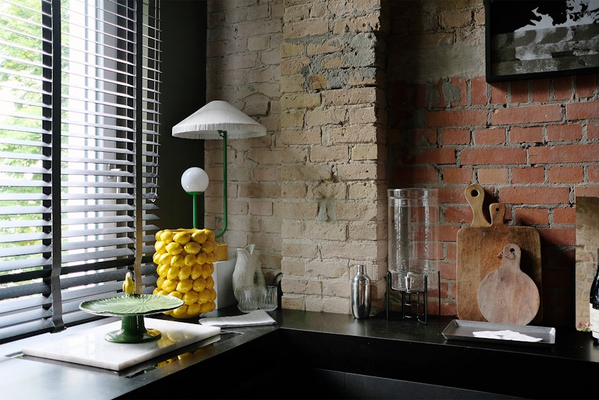 Dolce Vita in der Suite-Küche: italienische Keramik-Zitronenvase, Anrichteplatte mit Vogel, Tischleuchte von Gropius Lamps und freigelegte Backsteinwände 