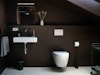 Minimalistisch und ein ganz besonderer Look für das neue Badezimmer – Die schräge Holzdecke sowie die Wände wurden im selben dunklen Farbton (Purple Brown, Little Greene) lackiert bzw. gestrichen, die weißen Elemente heben sich schön ab