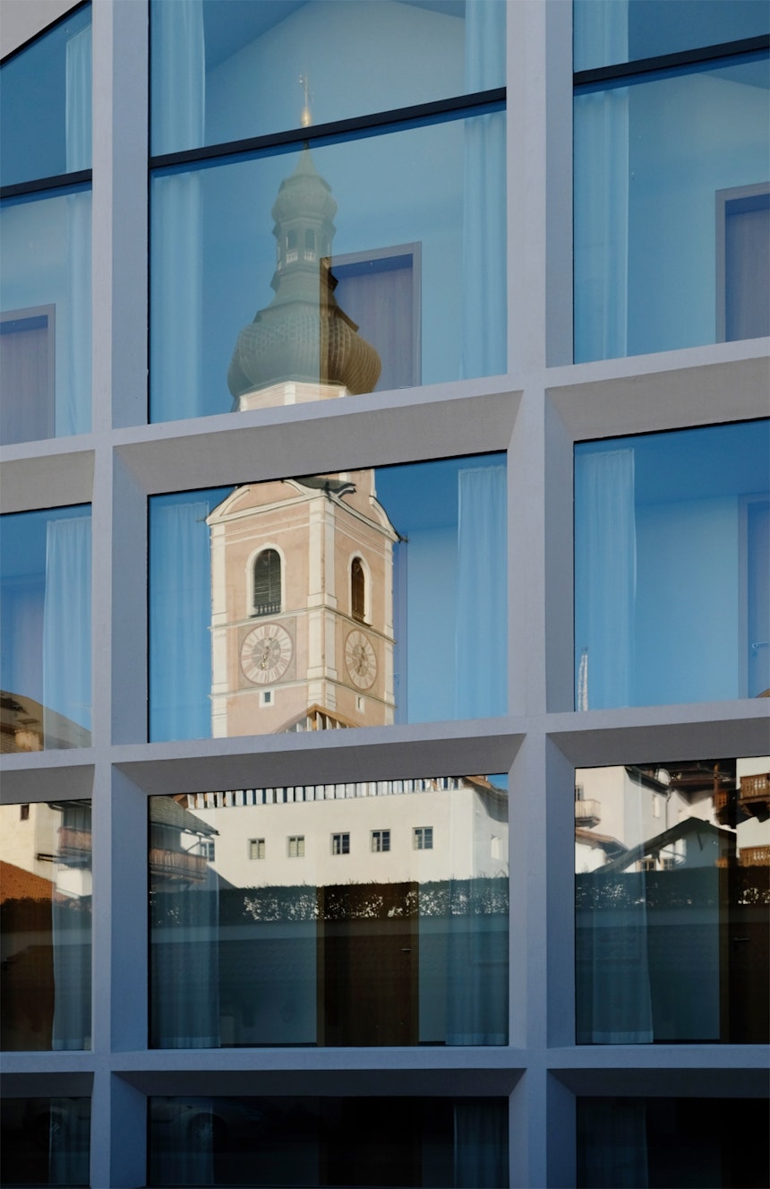 Klassizistik & Moderne – Der Kastelruther Kirchturm spiegelt sich in der Fassade des Hotels Schgaguler